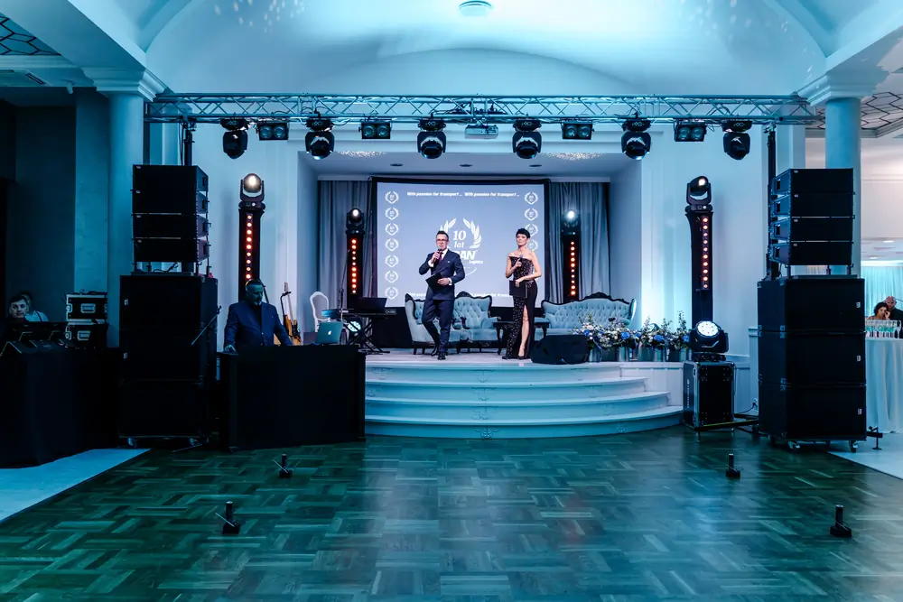 Gala jubileuszowa firmy: prowadzący na scenie, nagłośnienie liniowe i kratownica z oświetleniem