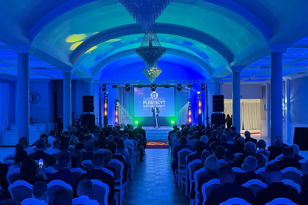 Konferencja w sali z kolumnami: scena z ekranem, nagłośnienie i oświetlenie